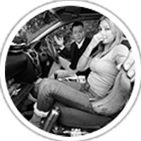 A woman sitting in a car holding her nose, indicating a bad smell, while a man reacts beside her.
