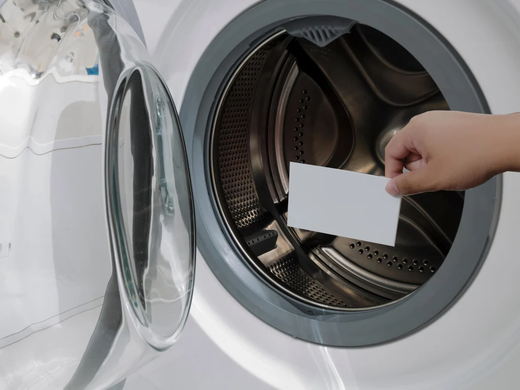 Hand placing a laundry detergent sheet into the drum of a front-loading washing machine